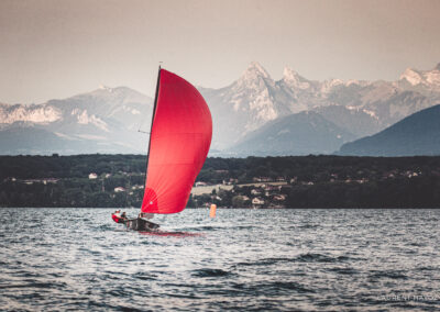 Equipage sous spinnaker rouge navigue sur le Lac Léman avec en arrière plan les montagne Dent D'Oche et Cornettes de Bise