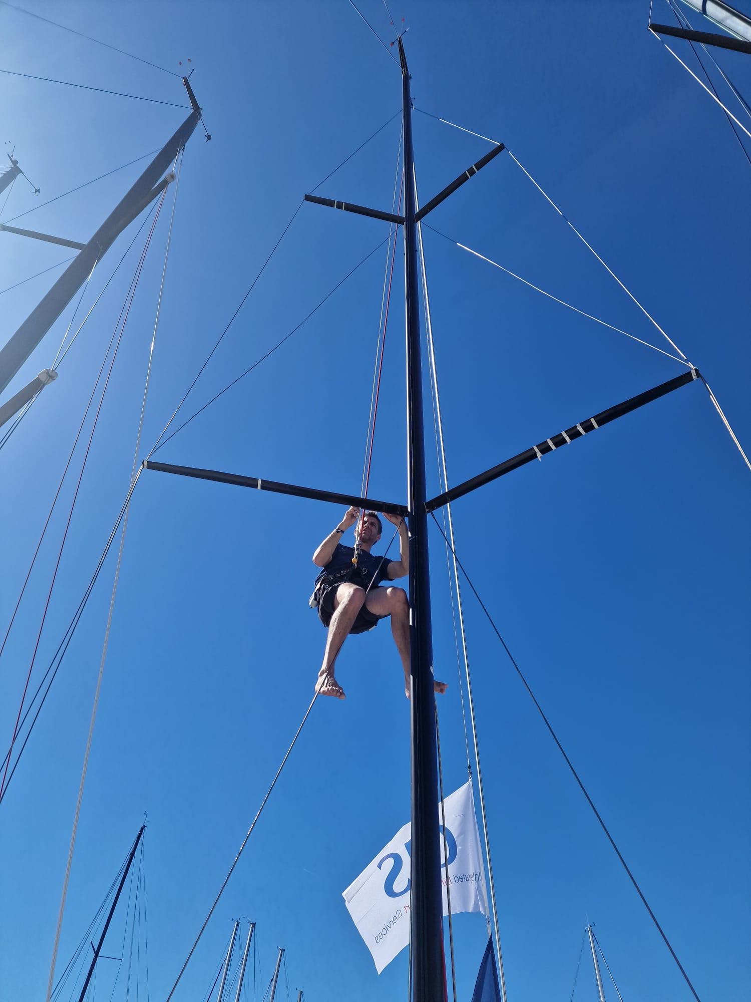 un équipier dans le mât pour coller des repères de réglages de voile d'avant
